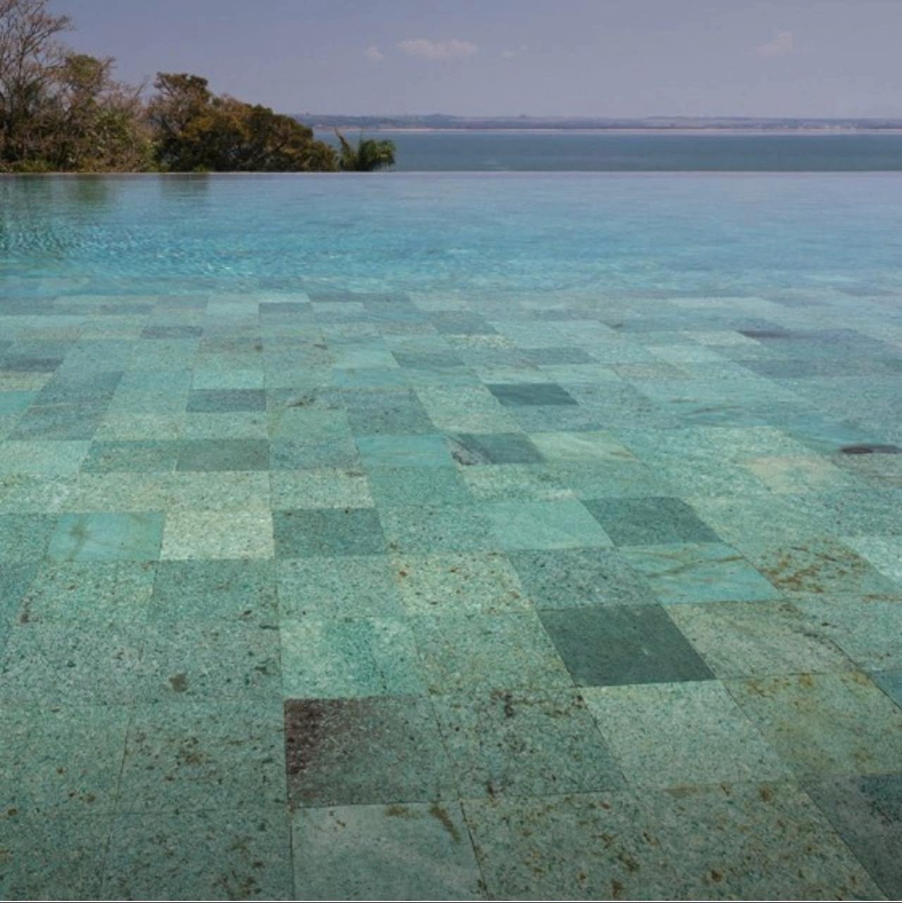 Piscina de borda infinita revestida com pedra verde, com vista para a lagoa
